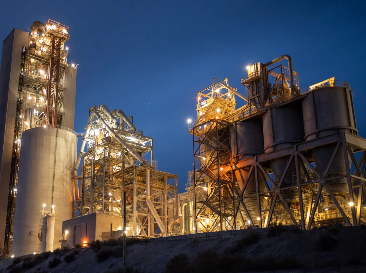 Fábrica com silos e estruturas metálicas iluminadas na hora azul