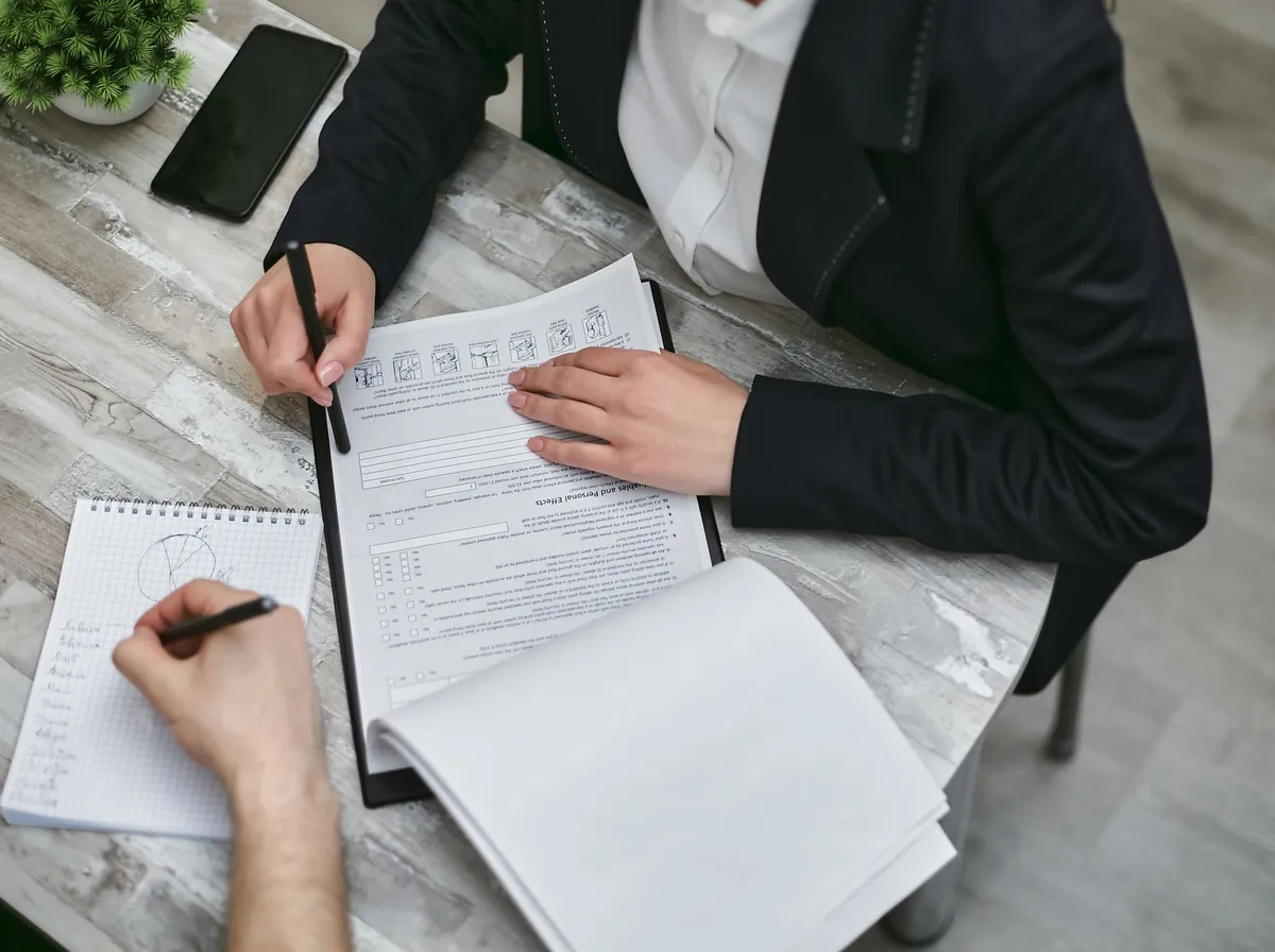 Duas pessoas revisando documentos sobre uma mesa, vistas de cima, só as mãos e os braços